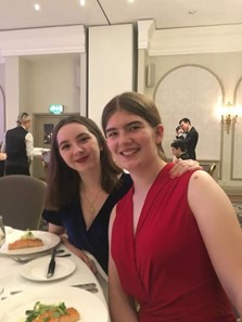 Annie (left) and Bethan (right) sat at a table with a white tablecloth in the Randolph hotel during the MedSoc Ball. A fillet of salmon is on Annie's plate. Both are smiling.