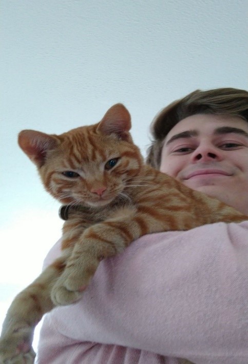 Arthur is smiling down at the camera, holding a white and orange striped cat which is also looking down at the camera.