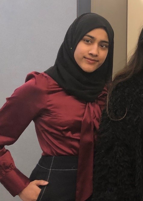 Nafisah is wearing a deep red top, and a black hijab. She is smiling at the camera.
