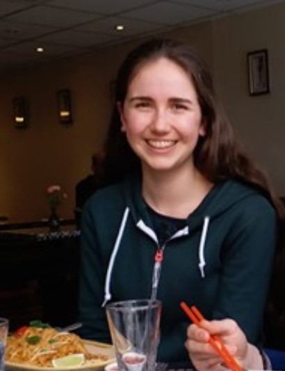 Seren wearing a dark green zipped up hoodie, with her hair down and smiling.